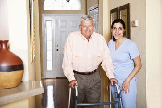 Home healthcare - Hispanic nurse at home of senior man (60s) using walker.