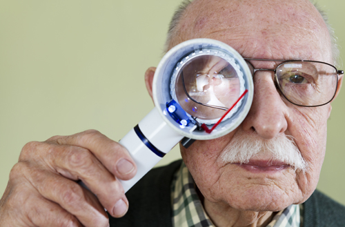 Senior man holding an illuminated magnifying glass.