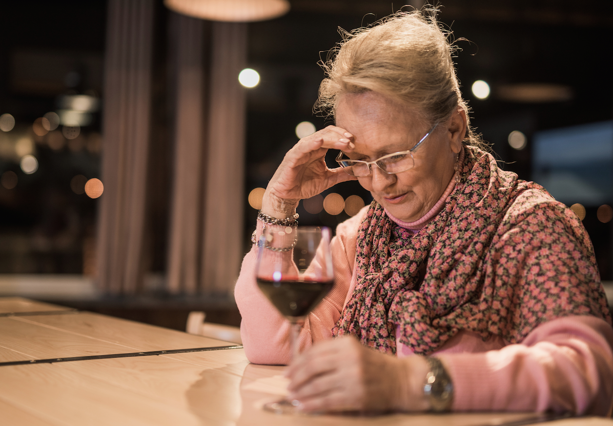 older woman sitting at bar with a glass of red wine